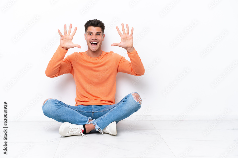 Young man sitting on the floor isolated on white background counting ten with fingers Young man sitting on the floor isolated on white background counting ten with fingers