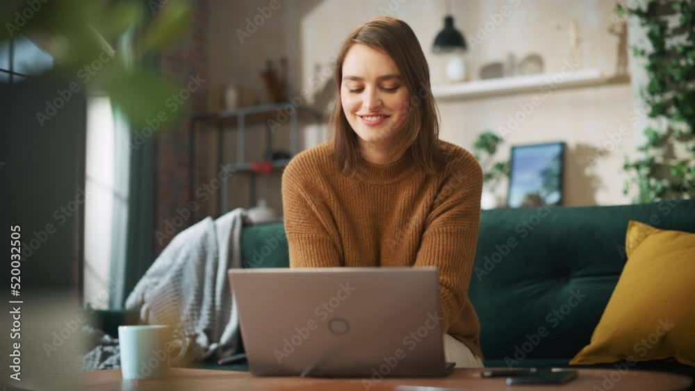 Portrait of Smiling Young Woman Working from Home on Laptop Computer in Sunny Cozy Apartment. Successful Creative Girl Entrepreneur Does Remote for e-Business Project, Online Shopping. Slow motion Portrait of Smiling Young Woman Working from Home on Laptop Computer in Sunny Cozy Apartment. Successful Creative Girl Entrepreneur Does Remote for e-Business Project, Online Shopping. Slow motion