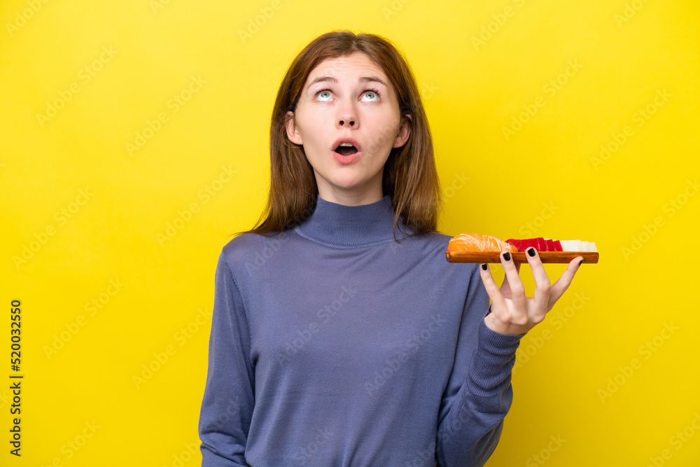 Young English woman holding sashimi isolated on yellow background looking up and with surprised expression Young English woman holding sashimi isolated on yellow background looking up and with surprised expression