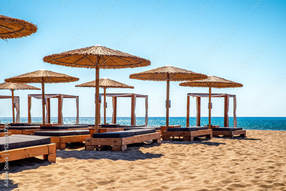 Empty loungers under sunshades on sandy beach with view on sea