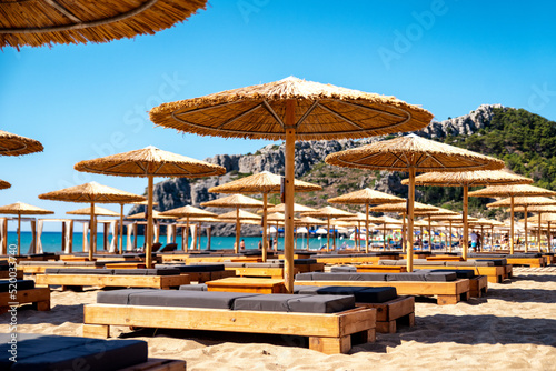 Loungers under sunshades ready for vacationers in Tsambika beach at Rhodes island in Greece