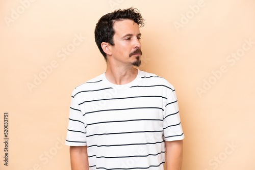 Young caucasian man isolated on beige background looking to the side