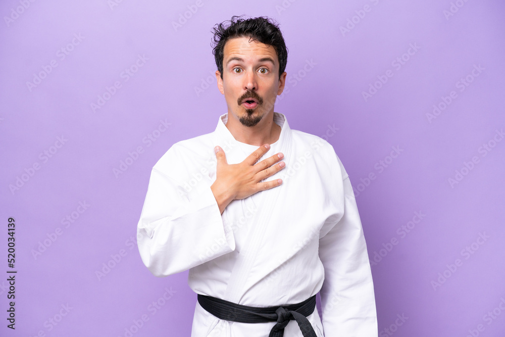 Young caucasian man doing karate isolated on purple background surprised and shocked while looking right Young caucasian man doing karate isolated on purple background surprised and shocked while looking right