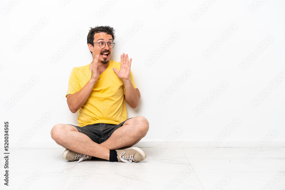 Young caucasian man sitting on the floor isolated on white background with surprise facial expression