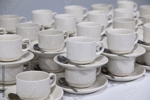 Serving for the company, catering, many white cups with silvery small spoons on a white table