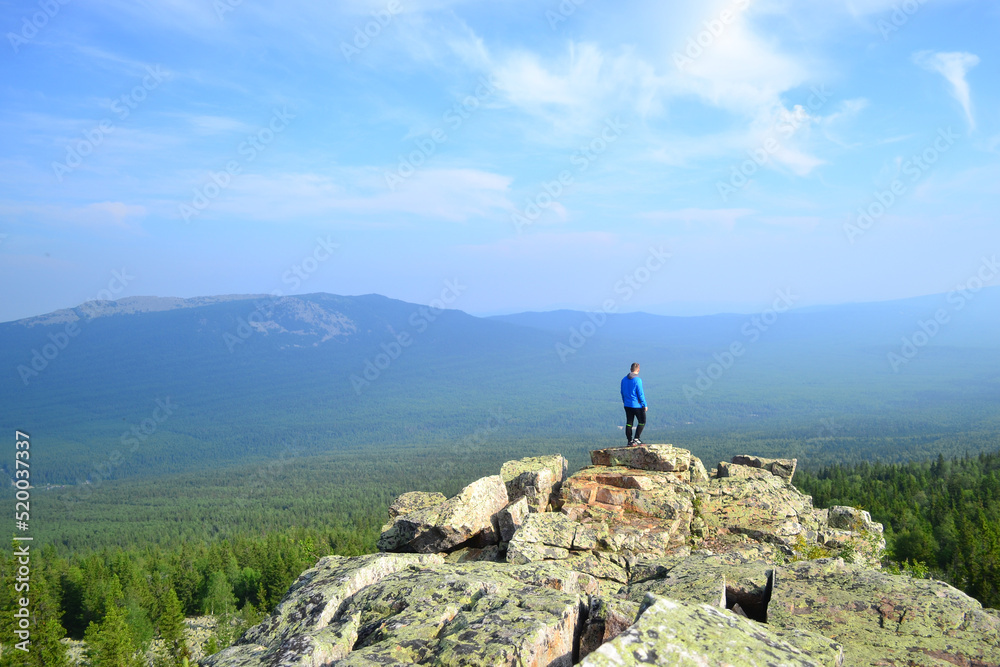 The guy stands on a cliff and looks into the distance at the mountains. Bright, sunny, low cloud day in the Urals