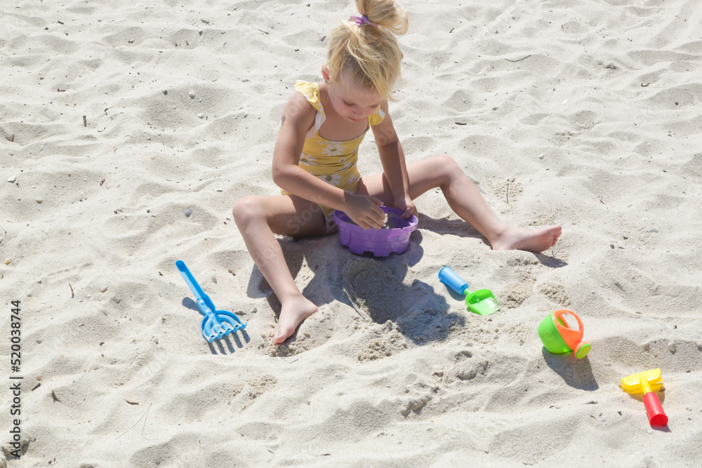 Cute happy 4 years old girl playing with plastic toys on the sandy beach. Cute happy 4 years old girl playing with plastic toys on the sandy beach.