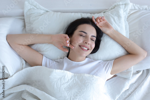 Top view, young beautiful brunette woman sleeping in bed with eyes closed, smiling in sleep wearing white t-shirt pajamas