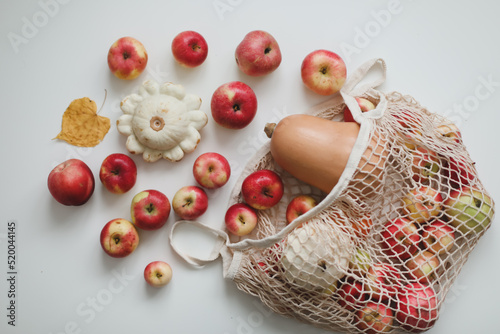 autumn harvest with sqush, pumpkin, apples and vegetables in a mesh shopping bag on white background photo