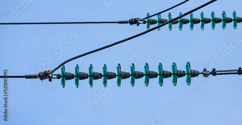 Close up of a transparent turquoise high voltage insulator or isolator in sunlight on electric tower on blue sky background. Electric power transmission line