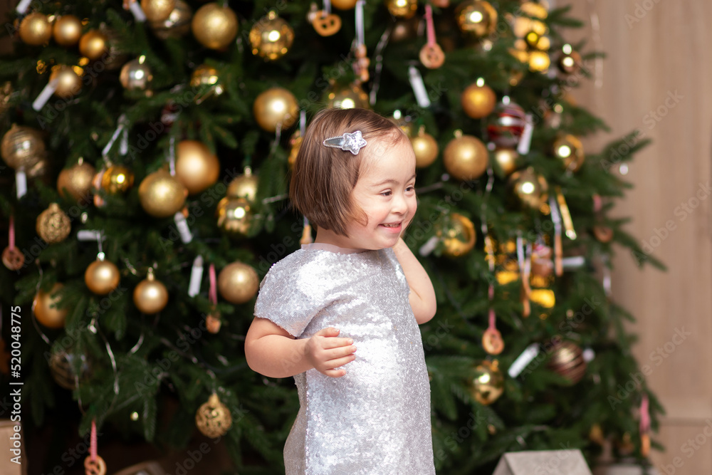 happy girl with down syndrome in a festive dress is standing near the Christmas tree, smiling, congratulations to special children happy girl with down syndrome in a festive dress is standing near the Christmas tree, smiling, congratulations to special children