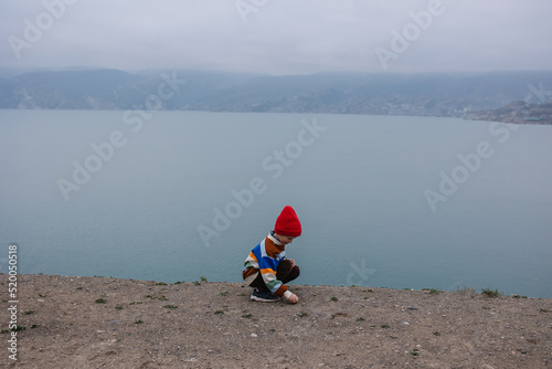free child plays in autumn in the mountains. Boy in a sweater and hat in winter on the coast. Loneliness away from everyone. Air atmosphere. Happy childhood. Traveling with children. Hiking and touris