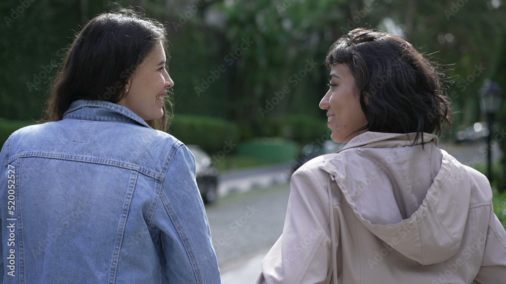 Two young female friends walking outside in street. Back of women talking and chatting on a walk Two young female friends walking outside in street. Back of women talking and chatting on a walk