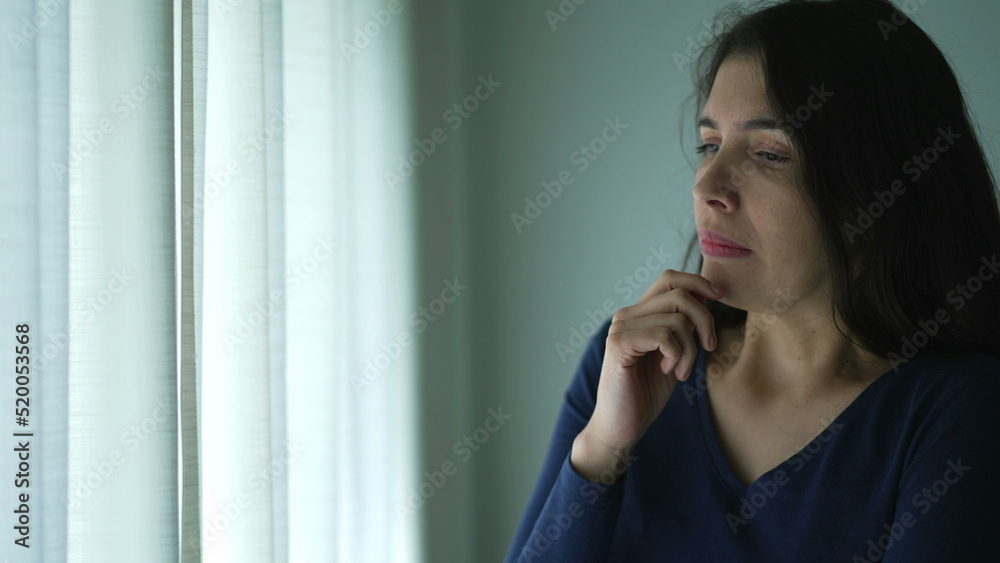 Preoccupied woman standing by window feeling anxiety Preoccupied woman standing by window feeling anxiety