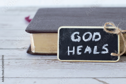 Foto God heals, a handwritten text written with chalk on a small blackboard with a closed Holy Bible Book in the background
