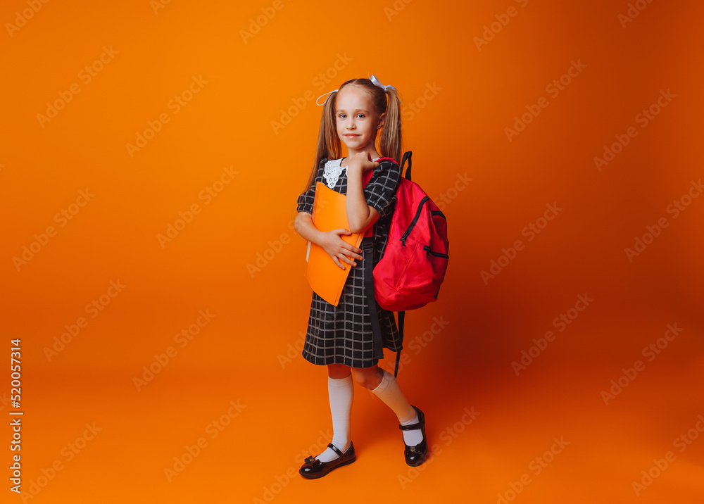 Back to school. A schoolgirl with a school bag on an isolated yellow studio background. a little girl holds a folder and a backpack.