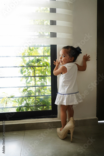 Niña feliz y traviesa con los zapatos tacones de su mamá jugando a ser grande, divertida posando y haciendo travesuras photo