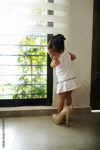 Niña feliz y traviesa con los zapatos tacones de su mamá jugando a ser grande, divertida posando y haciendo travesuras photo