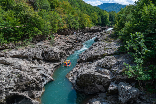 Group rafting and rowing on mountain on Belaya River. Happy tourists, men and women rafting accompanied by guide. Extreme sport. Russia, Republic of Adygea, Kamennomostsky settlement, August 15, 2020.