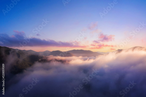 Mountains in low clouds. Mountain landscape with dramatic cloudy sky, peaks in fog and bright sunlight at dawn in the morning. Aerial view. Travel and tourism. © Артур Ничипоренко