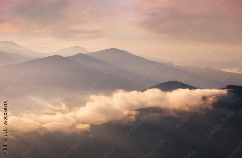 Mountains in low dense fog at morning sunrise. Beautiful landscape with mountain peaks in fog. Mountain valley in clouds. Mountains in low dense fog at morning sunrise. Beautiful landscape with mountain peaks in fog. Mountain valley in clouds.