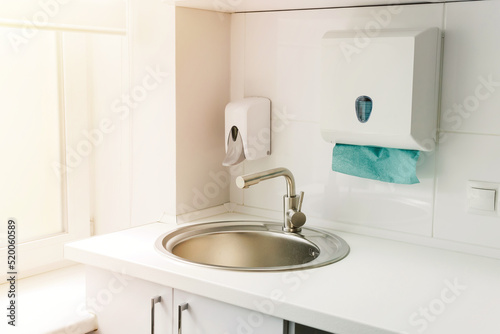 Modern hospital ward, hand washing sink, liquid soap disinfector automatic dispenser, paper towels, natural light.