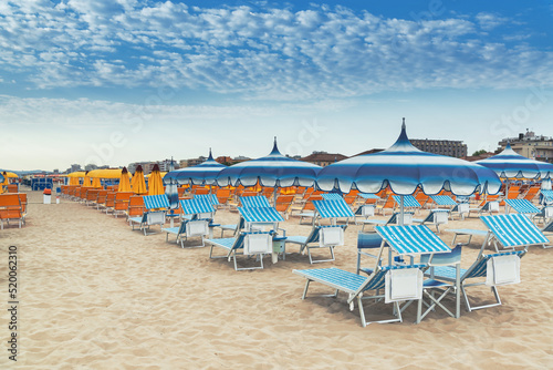 Fototapeta Naklejka Na Ścianę i Meble -  Beach in Rimini, Italy. Umbrellas on sandy beach in resort city Rimini on morning. Summer vacation to sea rest in Rimini