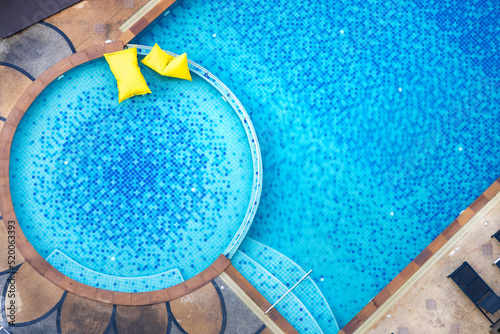Aerial view of yellow pool floating tube in blue swimming pool. High view from above.