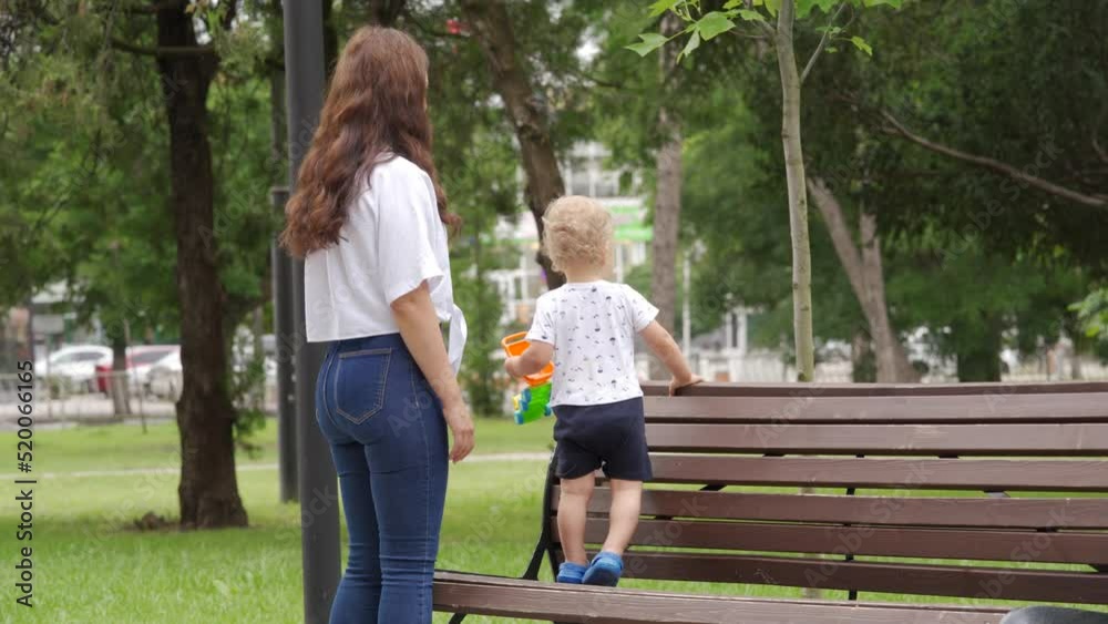 Mother and little child walk in the park in summer, toddler boy playing on a path on sunny day. Outdoor activity for children. Mother and little child walk in the park in summer, toddler boy playing on a path on sunny day. Outdoor activity for children.