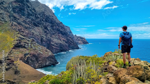 Backpack man on hiking trail from Afur to Taganana with scenic view of Atlantic Ocean coastline and Anaga mountain range, Tenerife, Canary Islands, Spain, Europe. Looking at Cabezo el Tablero crag