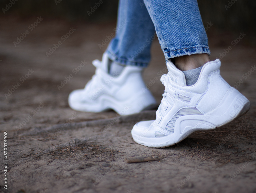 Fashionable white sneakers on female legs, close-up.