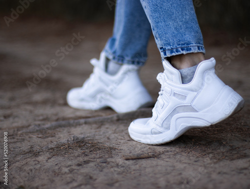 Fashionable white sneakers on female legs  close-up.