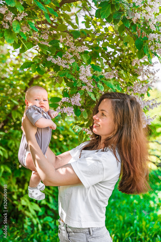Obraz premium Young beautiful mother and cute 3-month-old baby in lilac bushes in summer