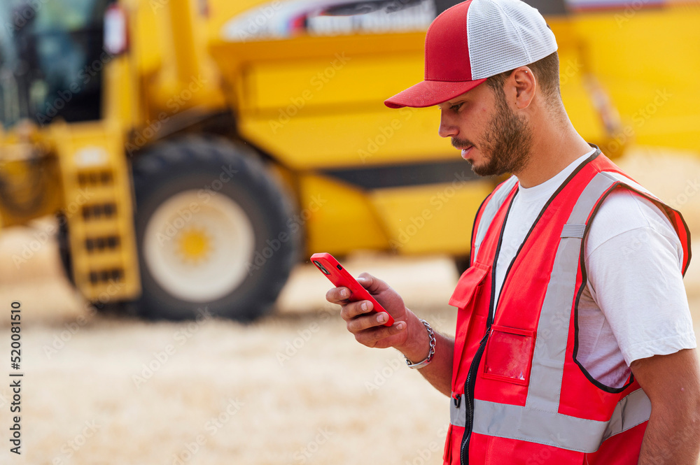 Concentrated man browsing smartphone near combine harvester Concentrated man browsing smartphone near combine harvester