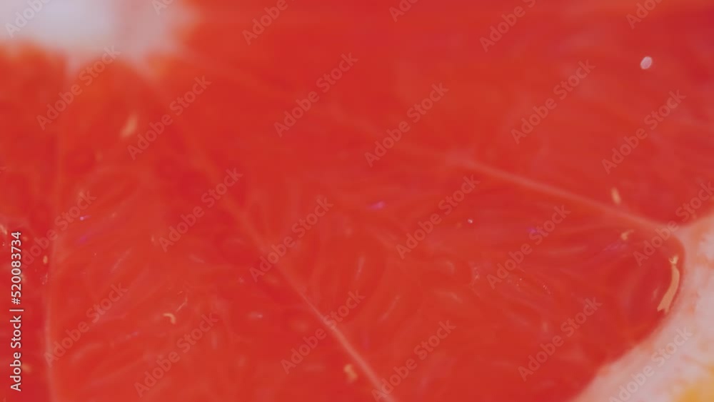 Colorful fresh red citrus fruit slice of grapefruit on slow rotating surface - close up view, macro, selective focus. Summer, tropical, natural, exotic and healthy food concept