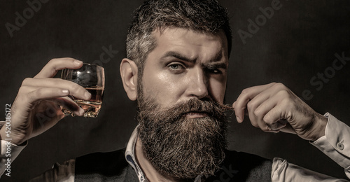 Tasting and degustation concept. Bearded businessman in elegant suit with glass of whiskey. Man drinking whiskey, brandy, cognac. Degustation, tasting