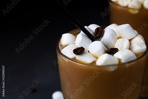 close-up with Tasty Ice coffee with marshmallow in a tall glass. Cold drink with coffee beans and ice on the black table. Cold summer drink on the black background with copy space.