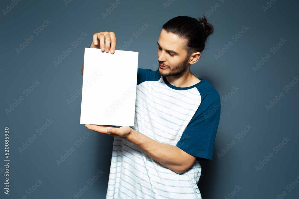 Studio portrait of guy holding white empty paper board on background of blue color. Studio portrait of guy holding white empty paper board on background of blue color.