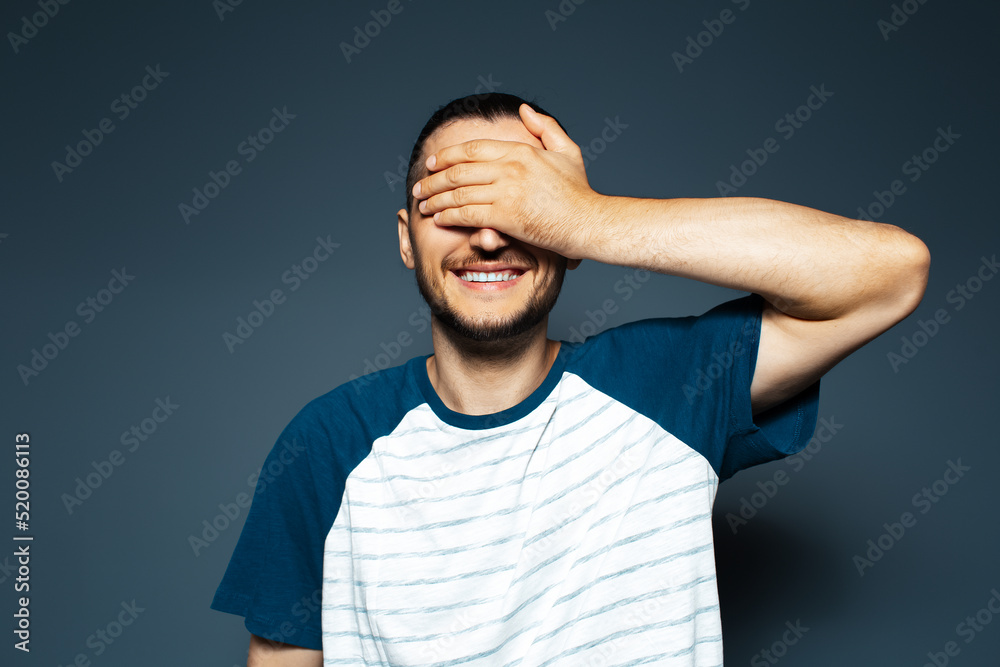 Studio portrait of young smiling man holding palm on face on blue background. Studio portrait of young smiling man holding palm on face on blue background.