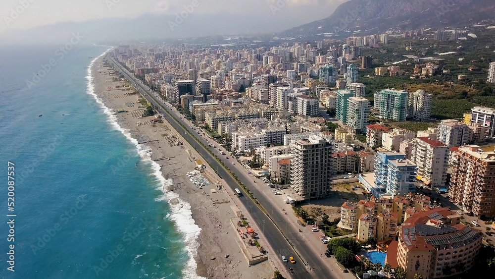 Top view of beautiful big city by sea on background of mountains. Clip. Panorama of southern resort town located on coast of blue sea and mountain landscape