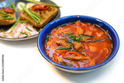 dish of ukrainian borsch with meat, bread and greens ready to eat on white background
