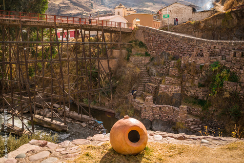 clay pot with river near stone construction and metal bridge in checacupe, cusco, peru photo