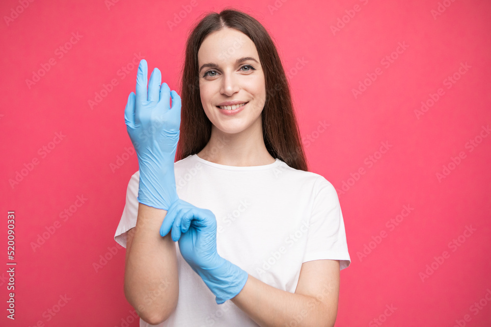 Young woman puts on protective surgical sterile gloves on her arm, isolated on pink background Young woman puts on protective surgical sterile gloves on her arm, isolated on pink background