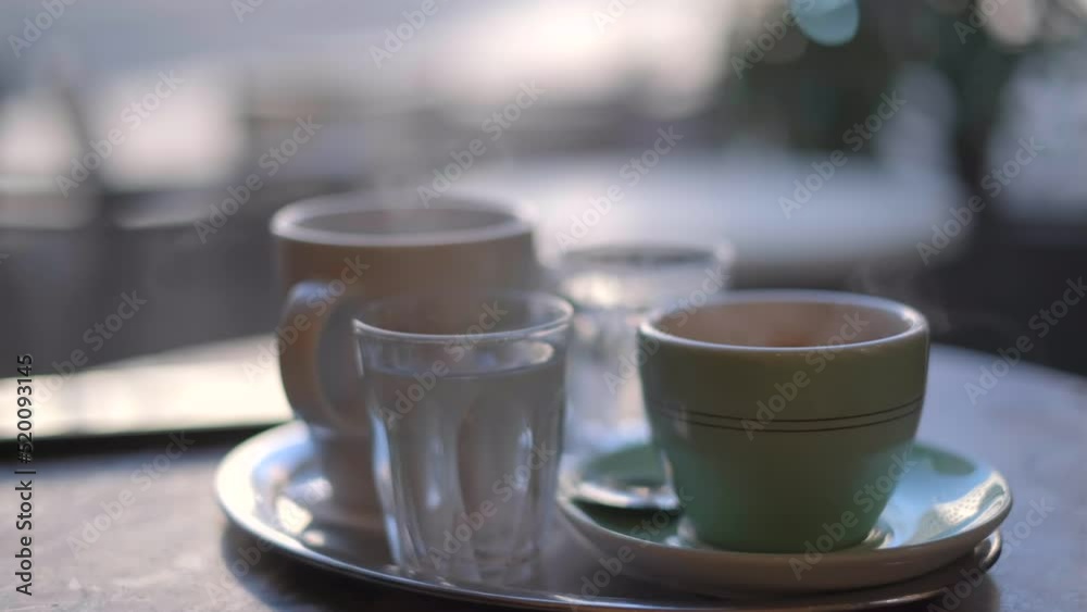Hot white coffee and tea in the cups with smoke on a table in cafe. Steaming hot coffee and tea cup with glass of water at the morning. Hot drink concept. High quality 4k footage Hot white coffee and tea in the cups with smoke on a table in cafe. Steaming hot coffee and tea cup with glass of water at the morning. Hot drink concept. High quality 4k footage