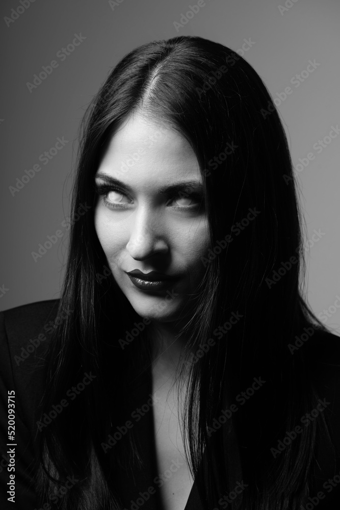 Beauty, make-up, horror and fashion concept. Sexy and beautiful woman with white eyes and long dark hair looking with uncomfortable and horrifying look. Model wearing black suit. Black and white image