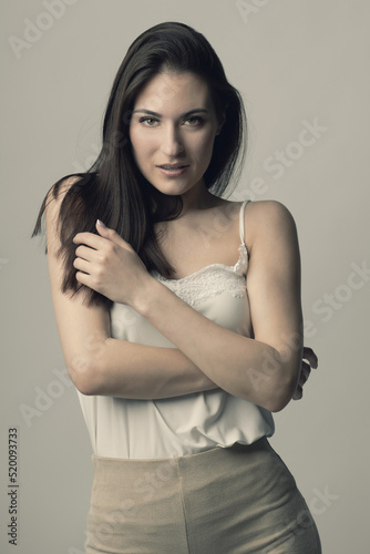 Fashion, style, beauty and make-up concept. Beautiful woman fashion studio portrait with long dark hair and day make-up with seductive look and pose with crossed arms. Toned image with beige color