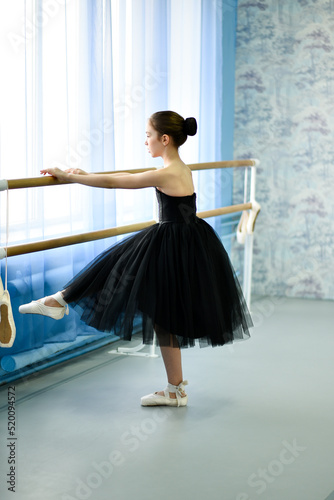 A beautiful girl ballerina in a black dress is engaged at the stonk. She's in a dance studio. Beauty. Dancing. Creation.