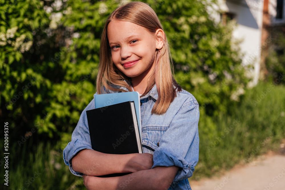 Smiling girl holding notebooks and looking at camera outdoor. Child ready for school. Back to school concept Smiling girl holding notebooks and looking at camera outdoor. Child ready for school. Back to school concept