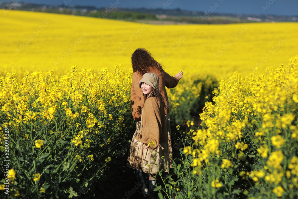 young mother and child daughter playing in the yellow rape fields. Family is having fun on the nature. Concept of friendly family and of summer vacation. mothers day and baby day. back view young mother and child daughter playing in the yellow rape fields. Family is having fun on the nature. Concept of friendly family and of summer vacation. mothers day and baby day. back view