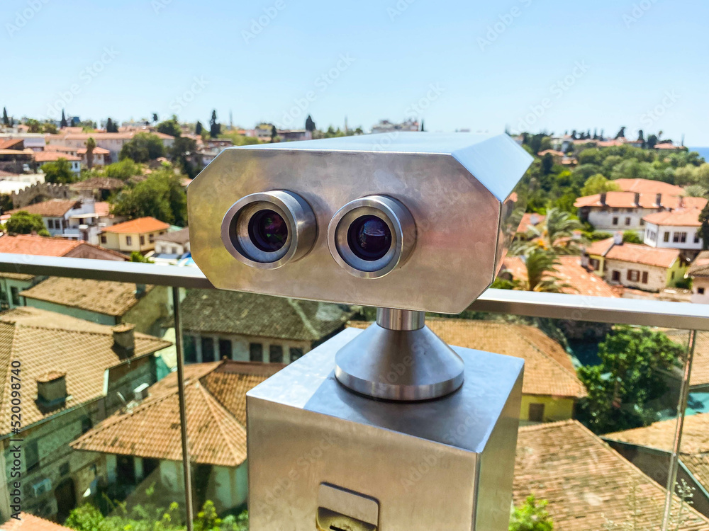 at the height of the houses of local residents with a tile roof. binoculars for tourists are installed on the roof. binoculars on a metal pedestal with black lenses